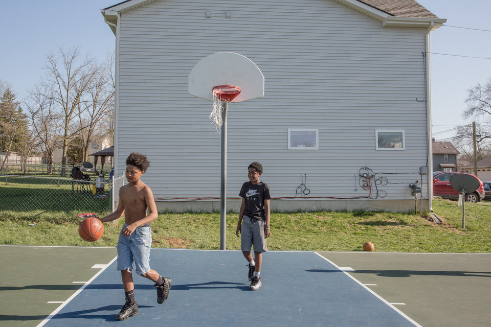 Two teenage boys play basketball outside on a community court.