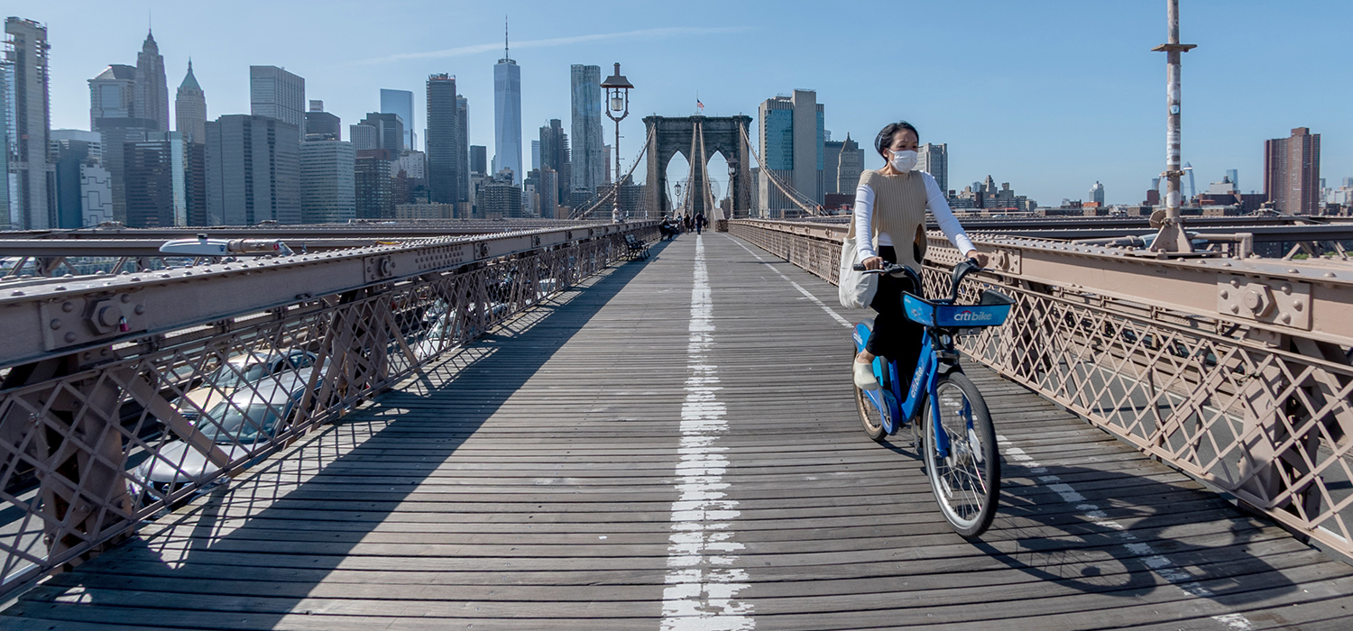 Woman wearing mask rides bike across Brooklyn Bridge