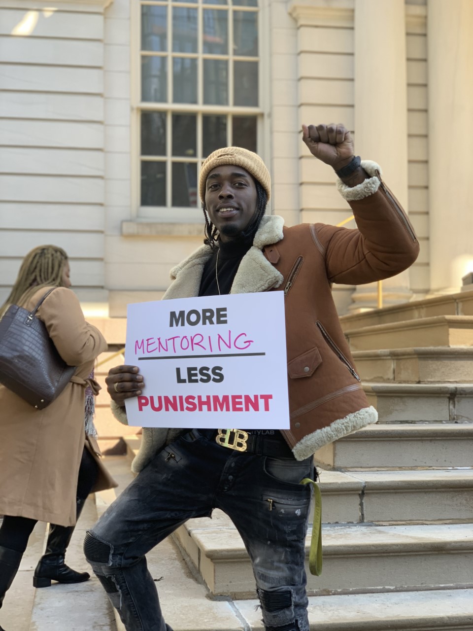 Man with fist raised holding 'more mentoring, less punishment' sign.