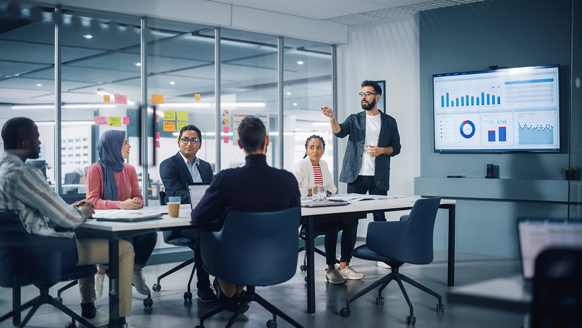 A man presenting graphs to a group of colleagues. 