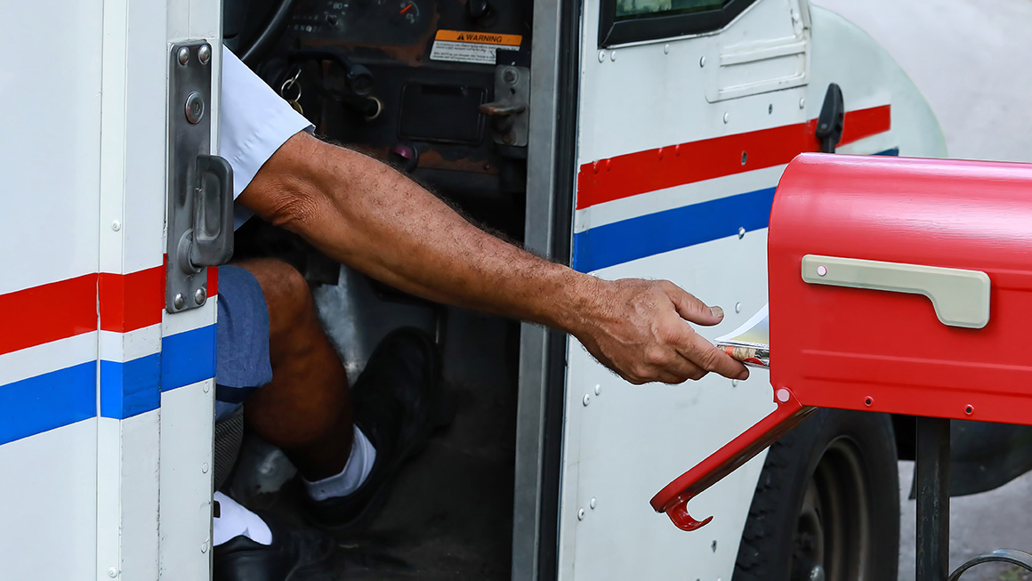photo of mail worker putting letter in mailbox