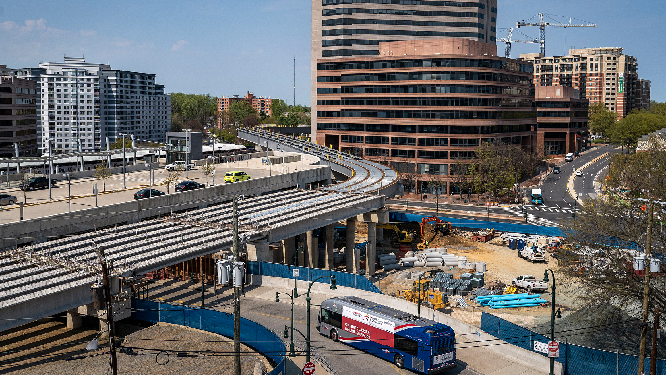 A bus drives under an underpass and beside a construction area