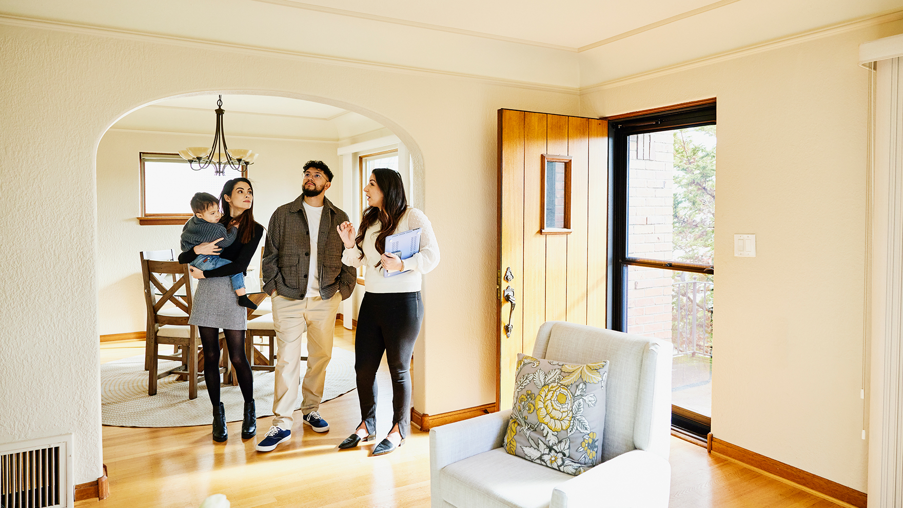 A young family stands in a living room looking at a house with a realtor.