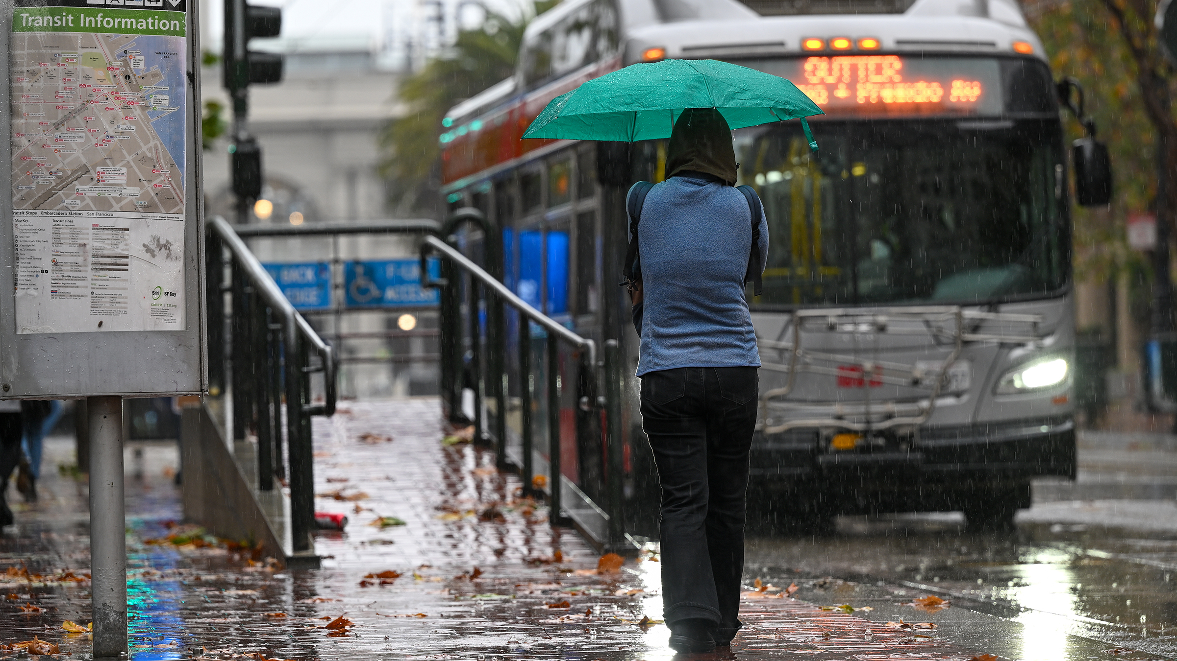 photo of a woman with umbrella waiting at a bus stop during rainy weather