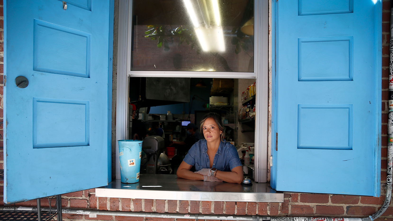 A woman working in a restaurant looks out a carry-out window at the camera