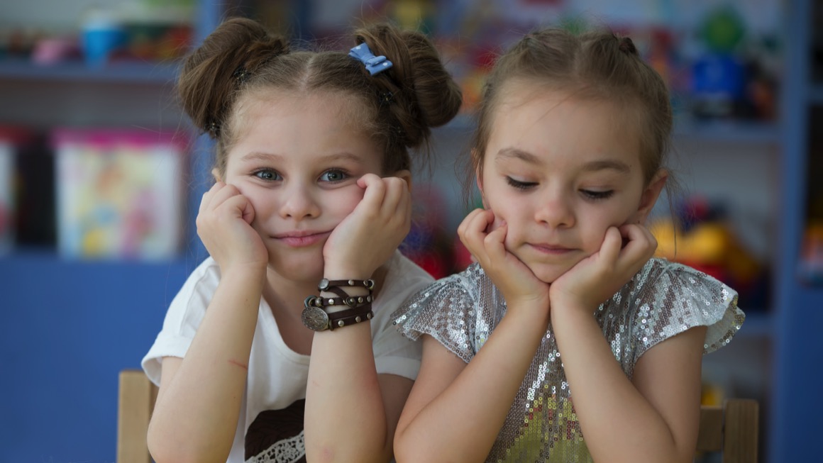 Two children hold their heads in their hands, one looks at the camera