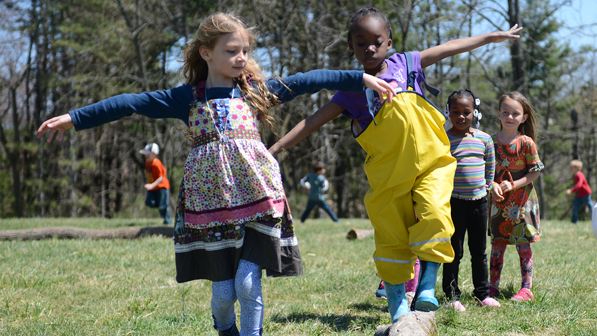 Two children play together outside, one walks on a balance beam