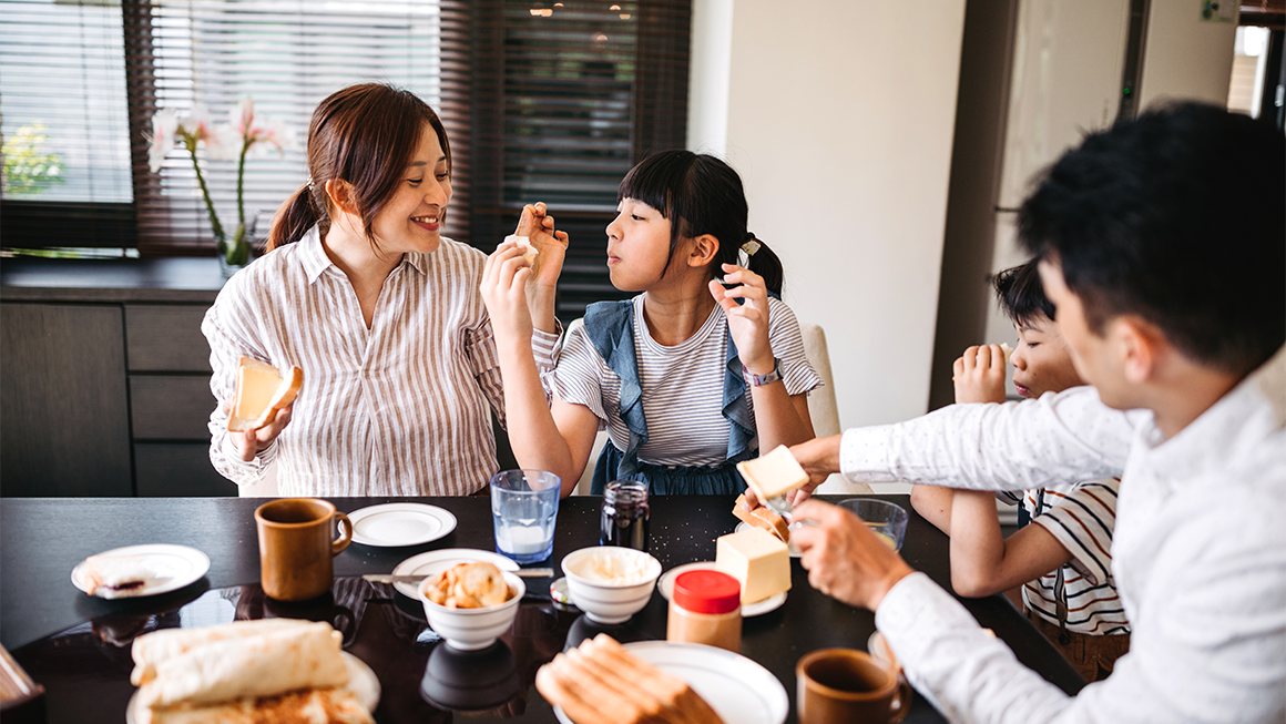    A group of four people sit around a bright dining table sharing a meal.