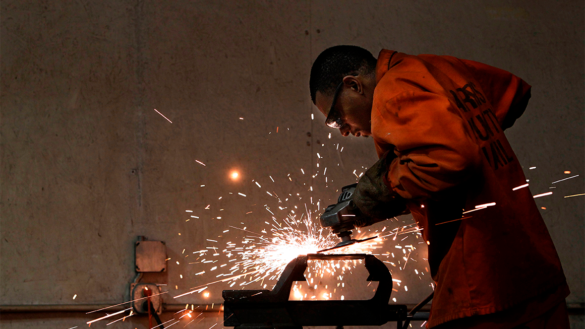 A man wearing an orange jumpsuit uses a tool, sparks fly