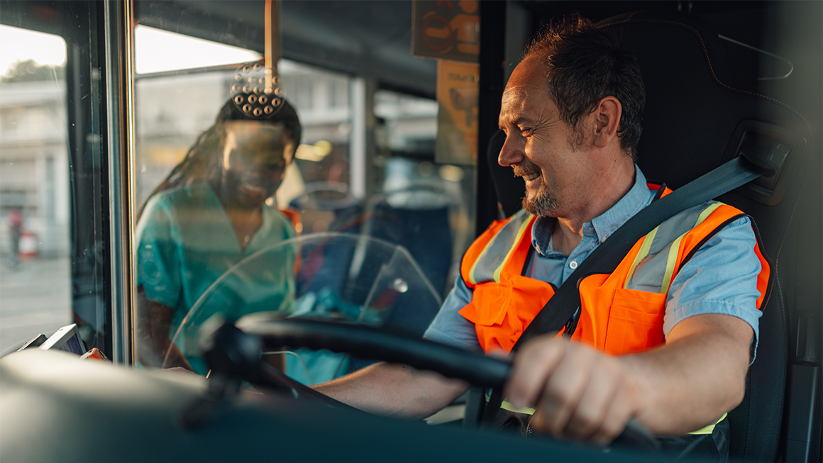A bus driver smiles while wearing an orange vest 