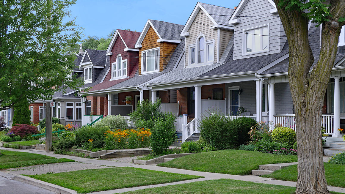 Row of colorful houses with porches and green lawns along a tree-lined street.