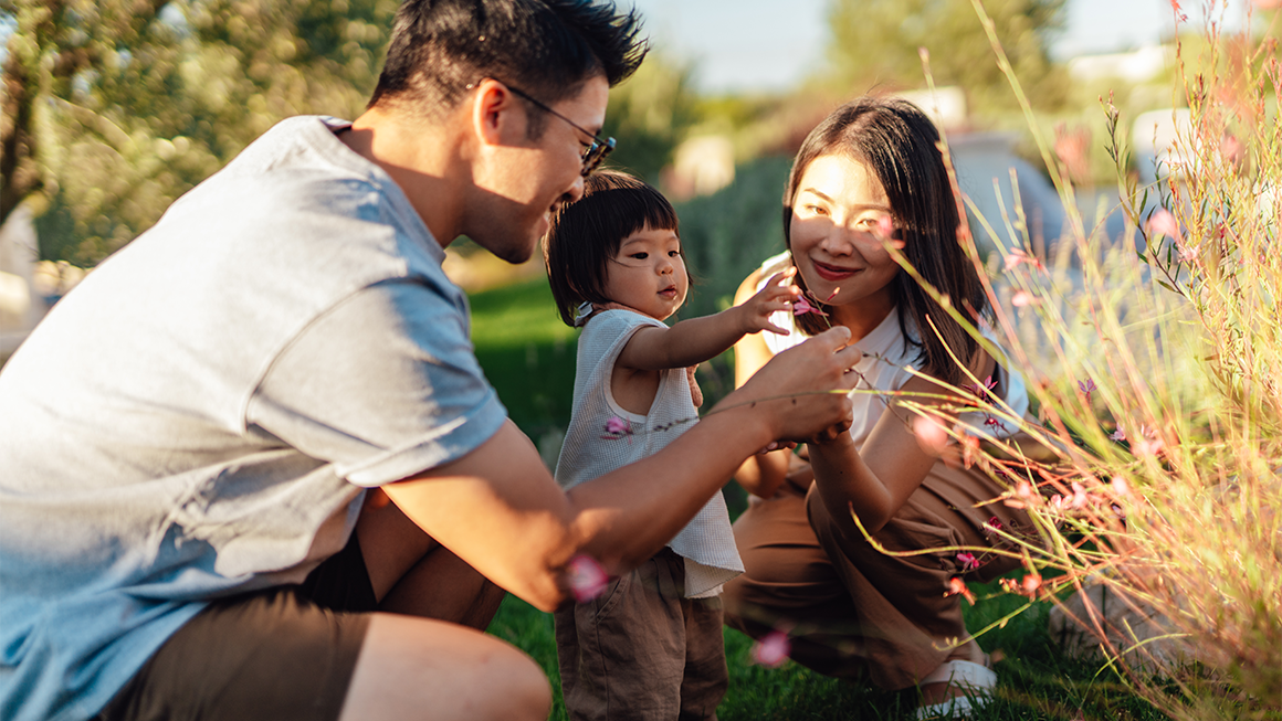 Photo of a young Asian American couple playing with their daughter outside.