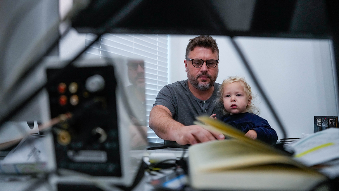A man holds a child on his lap while he uses a computer