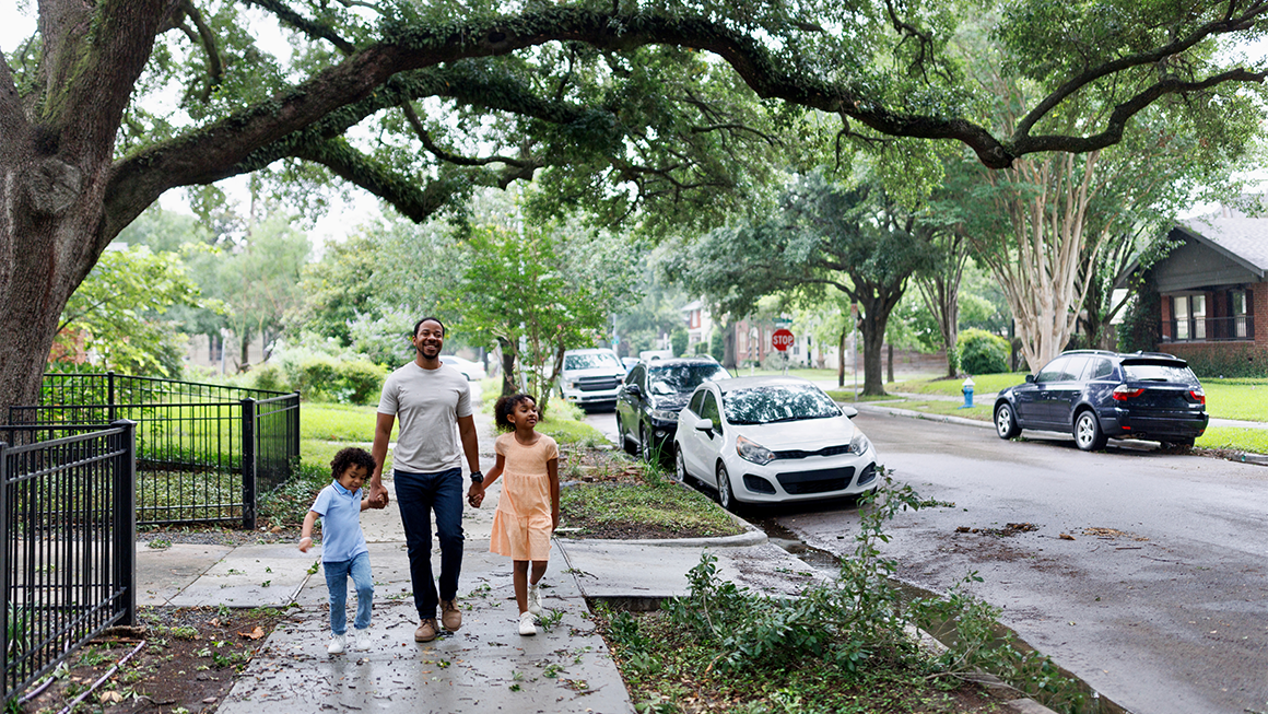Image of a young Black father smiling and walking his kids down the street.