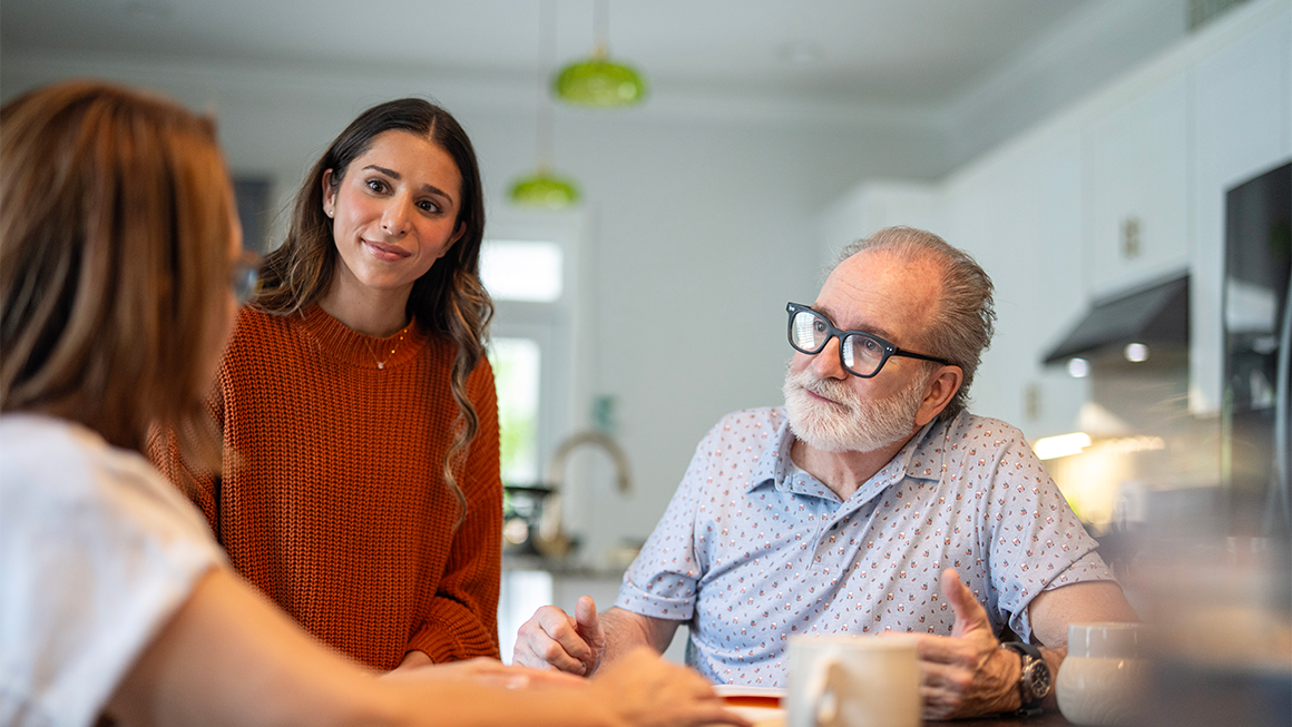 Photo of a young adult talking with her parents in their kitchen.