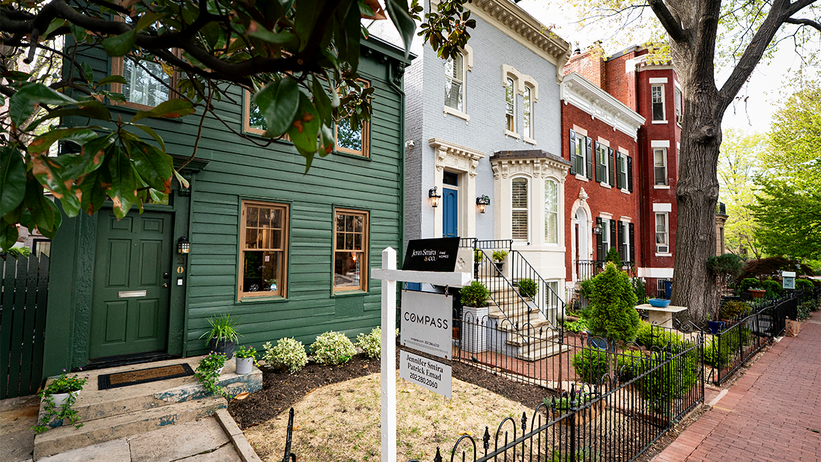 Several row houses, one with a Compass realty sign in the small front yard