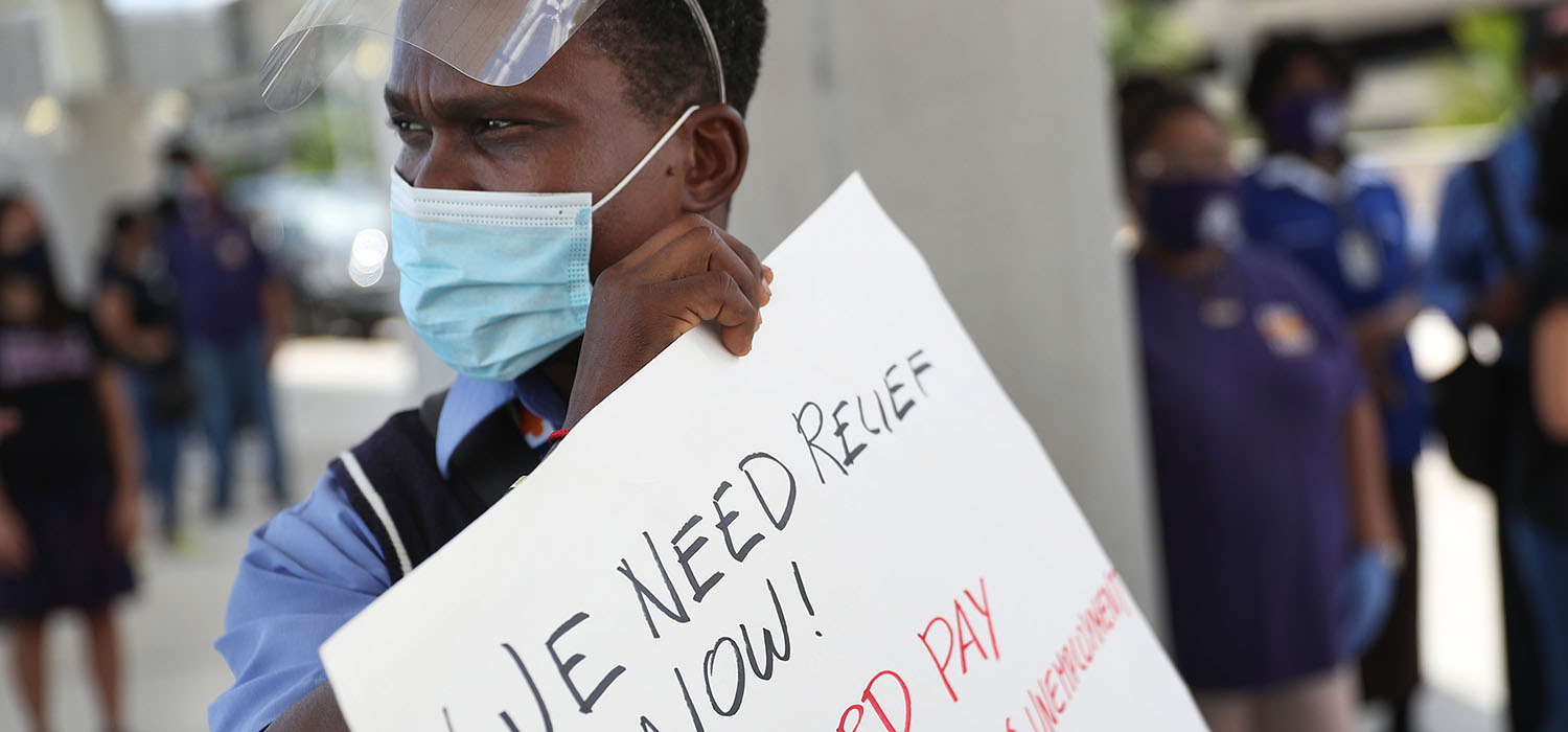 Protester holds a sign that reads, "we need relief now!"