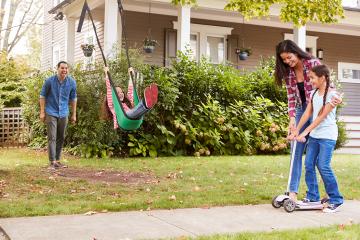 Children Playing On Garden Swing And Scooter Outside House
