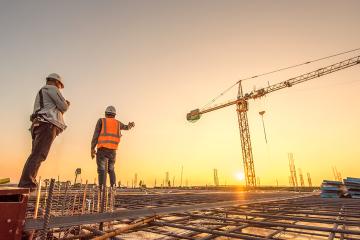 Construction engineers supervising progress of construction project stand on new concrete floor top roof and crane background