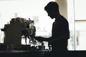 A silhouette profile of a barista working behind an espresso machine.