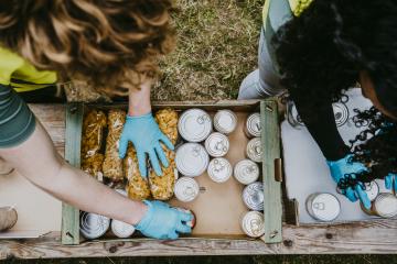  An overhead shot of two young people in turquoise gloves sorting and loading boxes of canned food and dried pasta.