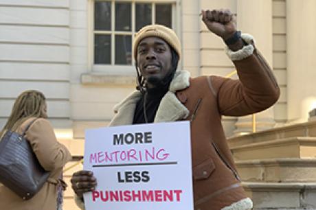 Man with fist raised holding "more mentoring, less punishment" sign.