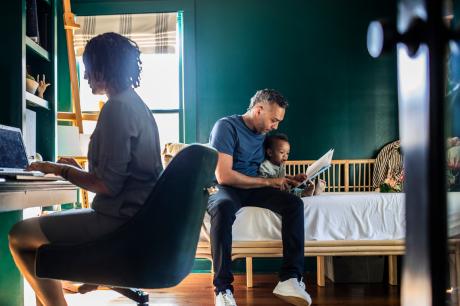 Father reading to baby as mother is on the computer.
