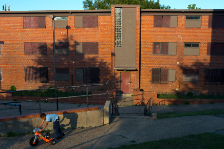 Child plays with a tricycle in front of a public housing building