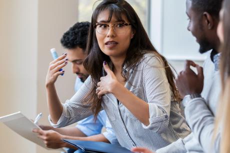 A woman with dark hair and glasses engages in a group discussion.
