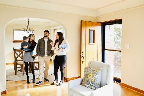 A young family stands in a living room looking at a house with a realtor.