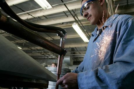 A man wearing safety glasses and a blue uniform works in a factory