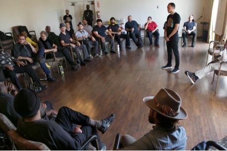 A group of men sits in chairs in a circle around one man in the middle
