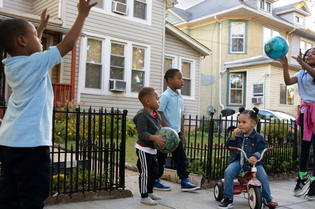Children play ball on a sidewalk outside some homes on a sunny day