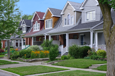 Row of colorful houses with porches and green lawns along a tree-lined street.