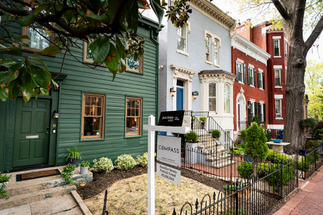 Several row houses, one with a Compass realty sign in the small front yard