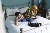 Two young adults on a bed playing with a cat.