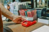 A man scans a credit card at a wooden counter. generic products in pink and blue are seen in the foreground.
