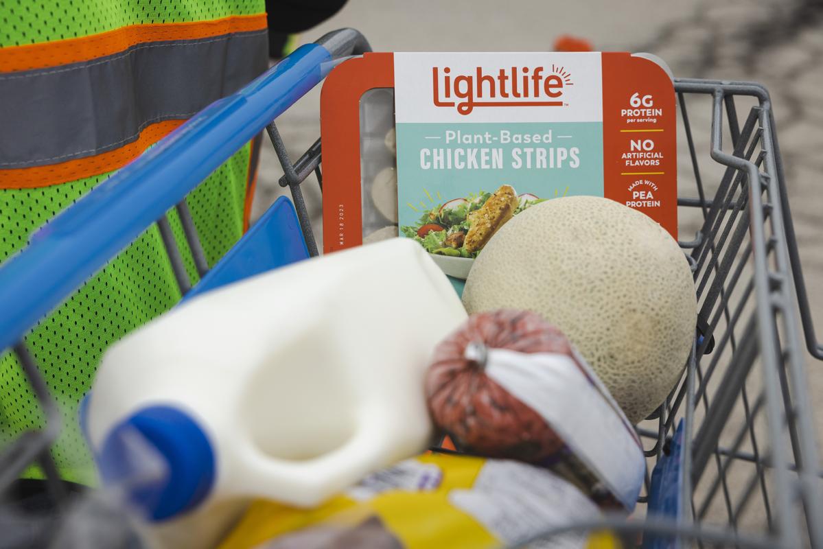 A grocery cart loaded with milk, chicken strips, sausage, and a melon. 